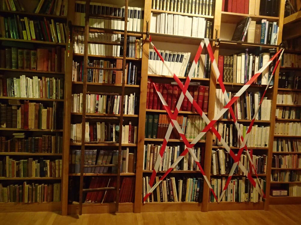 L’image montre une bibliothèque remplie de livres dont un pan est rendu indisponible par du ruban signalétique.